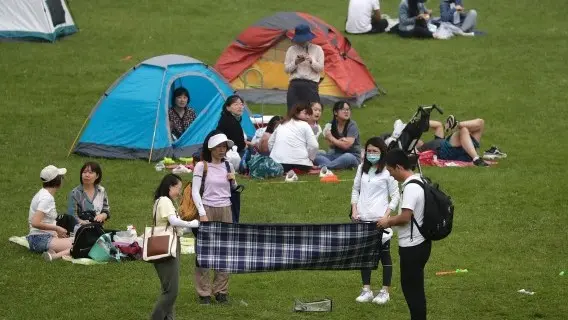 Woman wearing a face mask to help curb the spread of Covid-19 as her friends prepare to set up a picnic cloth on a scenic mountain in Yanqing, outskirt of Beijing, China