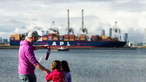 A masked man with his daughters look at a container ship in Melbourne