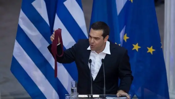 Greek Prime Minister Alexis Tsipras holds a tie he just removed at the end of a speech to celebrate the debt relief deal agreed by the country's creditors