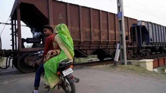 A man waits for a train carrying coal rakes to pass at a crossing, Dadri - May 2022