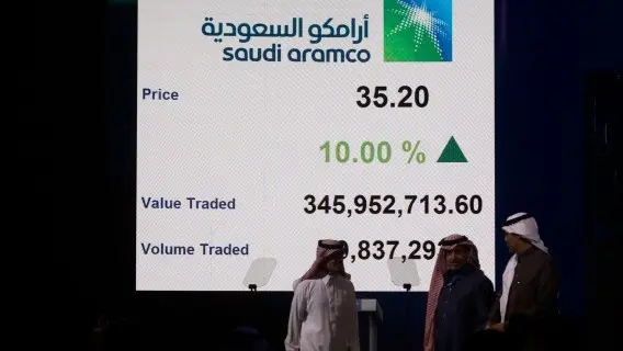 People walk past a screen displaying company details of Saudi Arabia's state-owned oil firm Armco in Riyadh