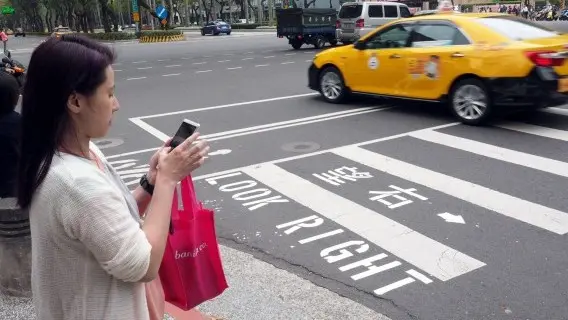 A woman checks her mobile phone while waiting to cross the street in Taipei, Taiwan